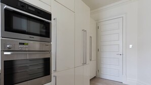 A kitchen with a built-in oven and a microwave, a white door, and light-colored cabinets. - Sloane Court East VI by onefinestay (London)