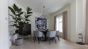 A dining area with a modern chandelier, a large abstract painting, and a potted plant. - Sloane Court East VI by onefinestay (London)