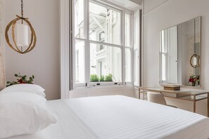 Hotellihuone, jossa on suuri sänky, peilillä varustettu työpöytä ja ikkuna, josta on näkymä rakennuksiin.