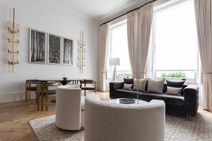 Een moderne woonkamer met een bank, een eettafel en een groot raam met gordijnen.