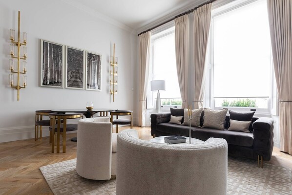 A modern living room with a sofa, a dining table, and a large window with curtains.