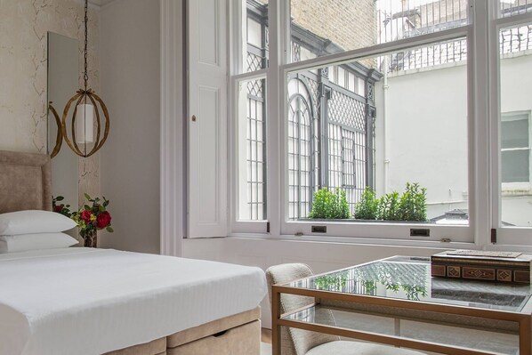 A bedroom with a bed, a glass table, and a view of the outside.