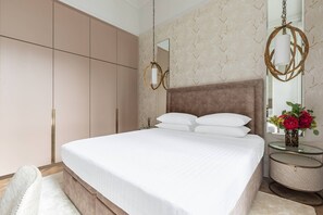 Een slaapkamer met een groot bed, een kledingkast, een ronde spiegel en een klein tafeltje met bloemen.