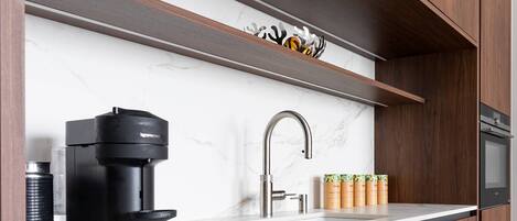 Une cuisine moderne dotée d’une machine à expresso intégrée, d’un robinet en acier inoxydable et d’un meuble en bois placé au-dessus du plan de travail.