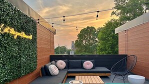 An outdoor seating area with a green wall, a black sofa with patterned cushions, a wooden table, and a metal chair. - Modern Group Oasis w/ Private Rooftop Deck, Steps to FedExForum (Memphis)