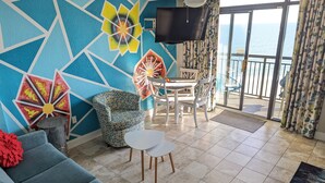 Un salon doté d’une grande fenêtre, d’un téléviseur et d’un balcon offrant une vue sur la mer.