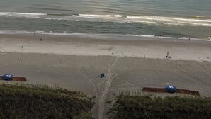 Une plage avec un arc-en-ciel, une mer calme et quelques personnes.