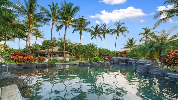 A tranquil pool area with clear water, surrounded by palm trees and a small waterfall. - Mauna Lani Beach Club Pass included!  Palm Villas B4 (Waimea)