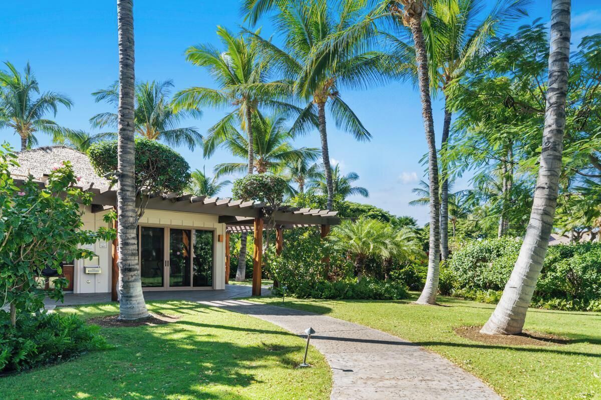 A resort with a covered outdoor area, palm trees, and a well-maintained lawn.
