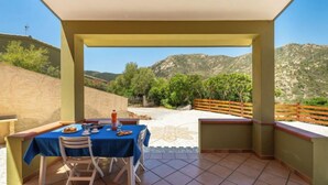 A covered outdoor dining area with a table set for two, overlooking a mountainous landscape. - Vacation home Luli by Interhome (Villasimius)