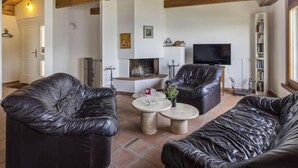 Una sala de estar con vigas de madera, chimenea, televisor y sofás de cuero.
