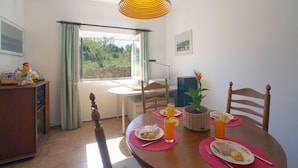 A dining area with a table set for two, a window with curtains, a wooden cabinet, and a hanging lamp. - Vacation home Vista by Interhome (São Bartolomeu de Messines)