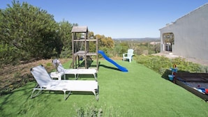 A backyard with a wooden play structure, a blue slide, and two white lounge chairs. - Vacation home Vista by Interhome (São Bartolomeu de Messines)