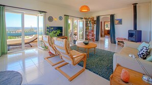 Amplia sala de estar con televisor grande, chimenea, estantería y comedor con sillas y mesa.