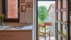 A room with a brick wall, a window, a television, and a door leading to an outdoor area with a chair and a table. - Casa Dascio by Interhome (Sorico Albonico)