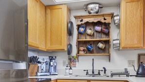 Une cuisine avec des meubles de rangement en bois, un réfrigérateur en acier inoxydable, une machine à café et une étagère où sont posées des tasses.