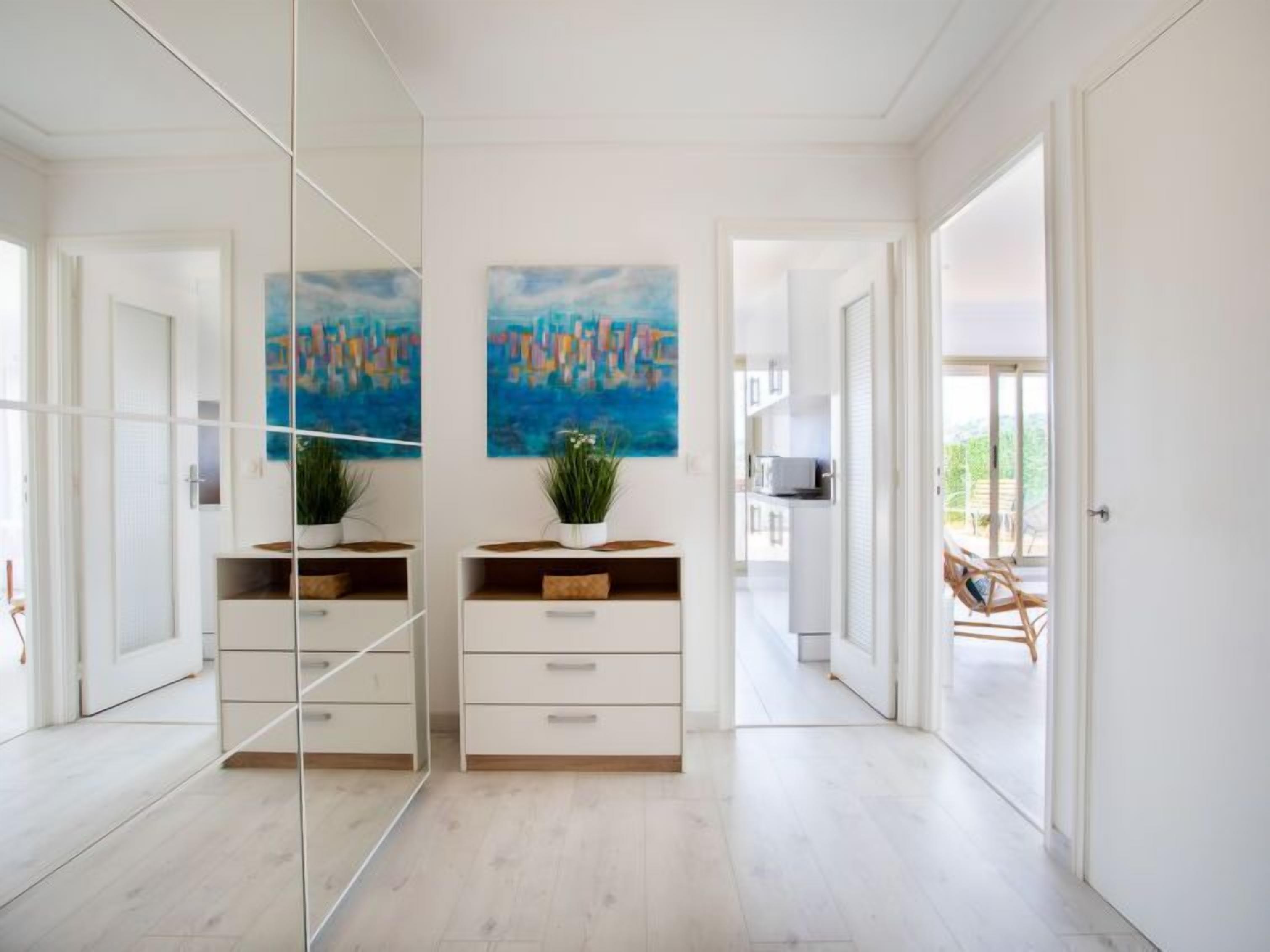 A modern interior with a mirrored wardrobe, two abstract paintings, a potted plant, and a view of a balcony with outdoor furniture.