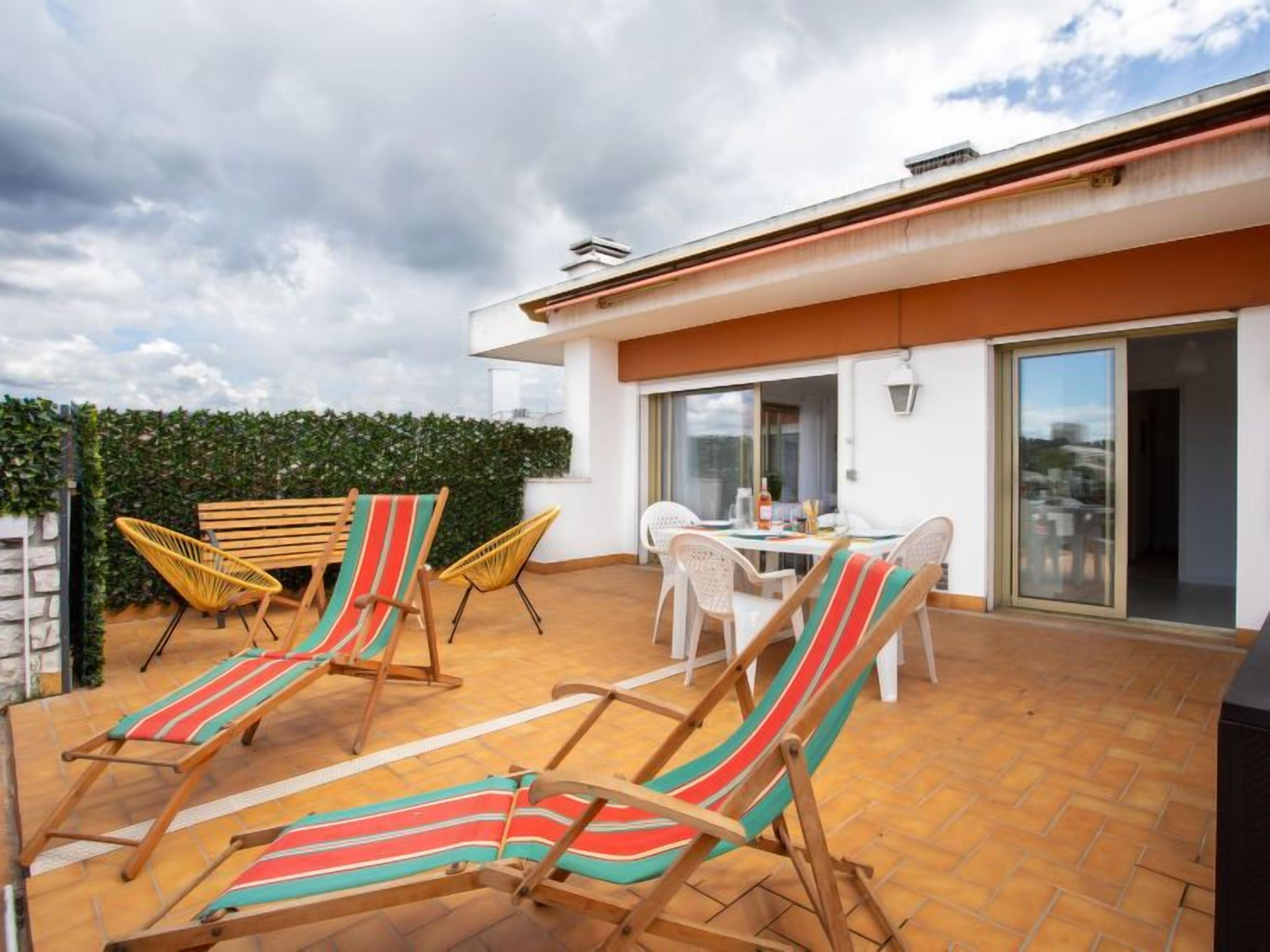 A rooftop terrace with lounge chairs, a dining table, and a view of the cityscape.