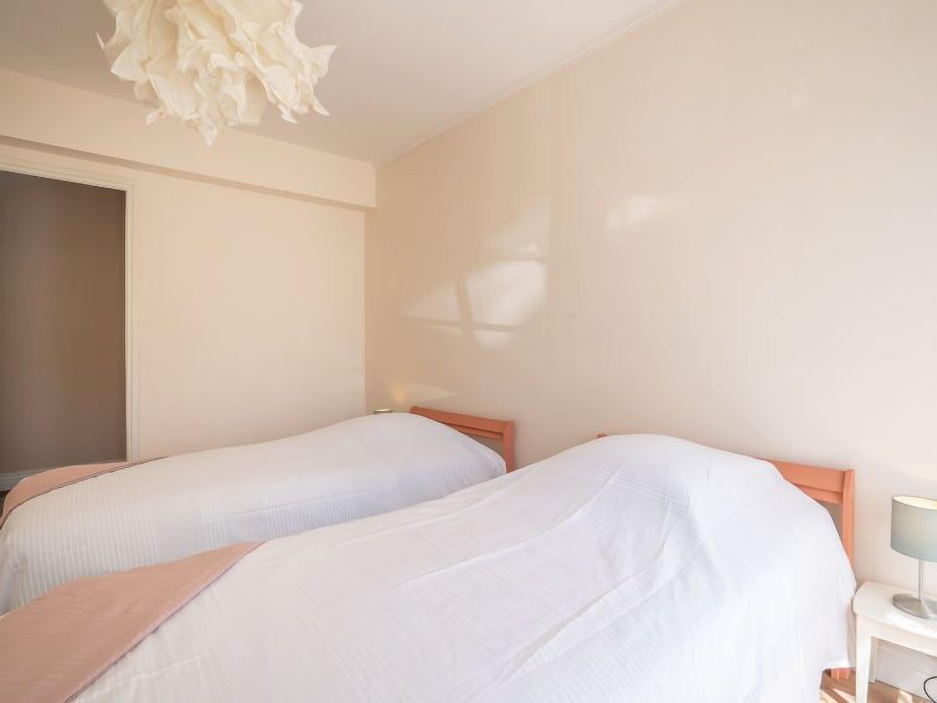 A hotel room with two single beds, a bedside table with a lamp, and a ceiling light fixture.