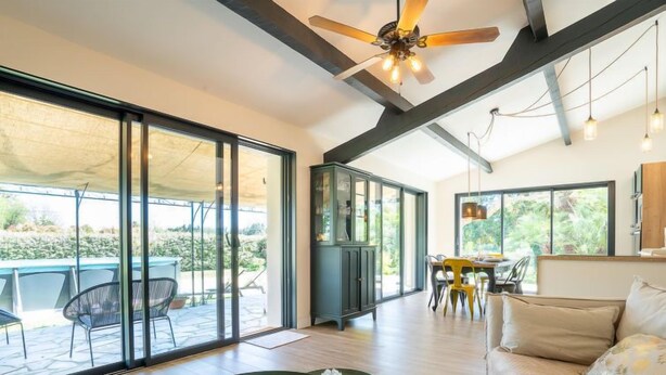 Amplia sala de estar con puerta de vidrio que da a un patio exterior, ventilador de techo y comedor con mesa y sillas.