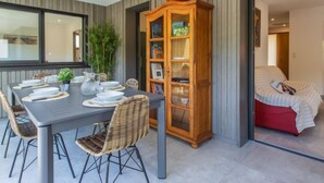 Un coin repas avec une table dressée pour six personnes, entouré de chaises en osier, d’un buffet en bois aux portes vitrées et d’un grand miroir accroché au mur.