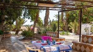 En udendørs terrasse med et spisebord, omgivet af stole og overdækket af en pergola.