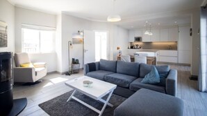 A modern living room with a grey sofa, a white coffee table, and a TV. There is a kitchen in the background with white cabinets and a microwave. - Beautiful detached Villa, 10 minutes walk from Porto Do Mos beach (Lagos)