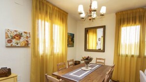 A dining room with a wooden table, chairs, yellow curtains, a chandelier, and artwork on the walls. - Ca La Lou by Interhome (Sils)