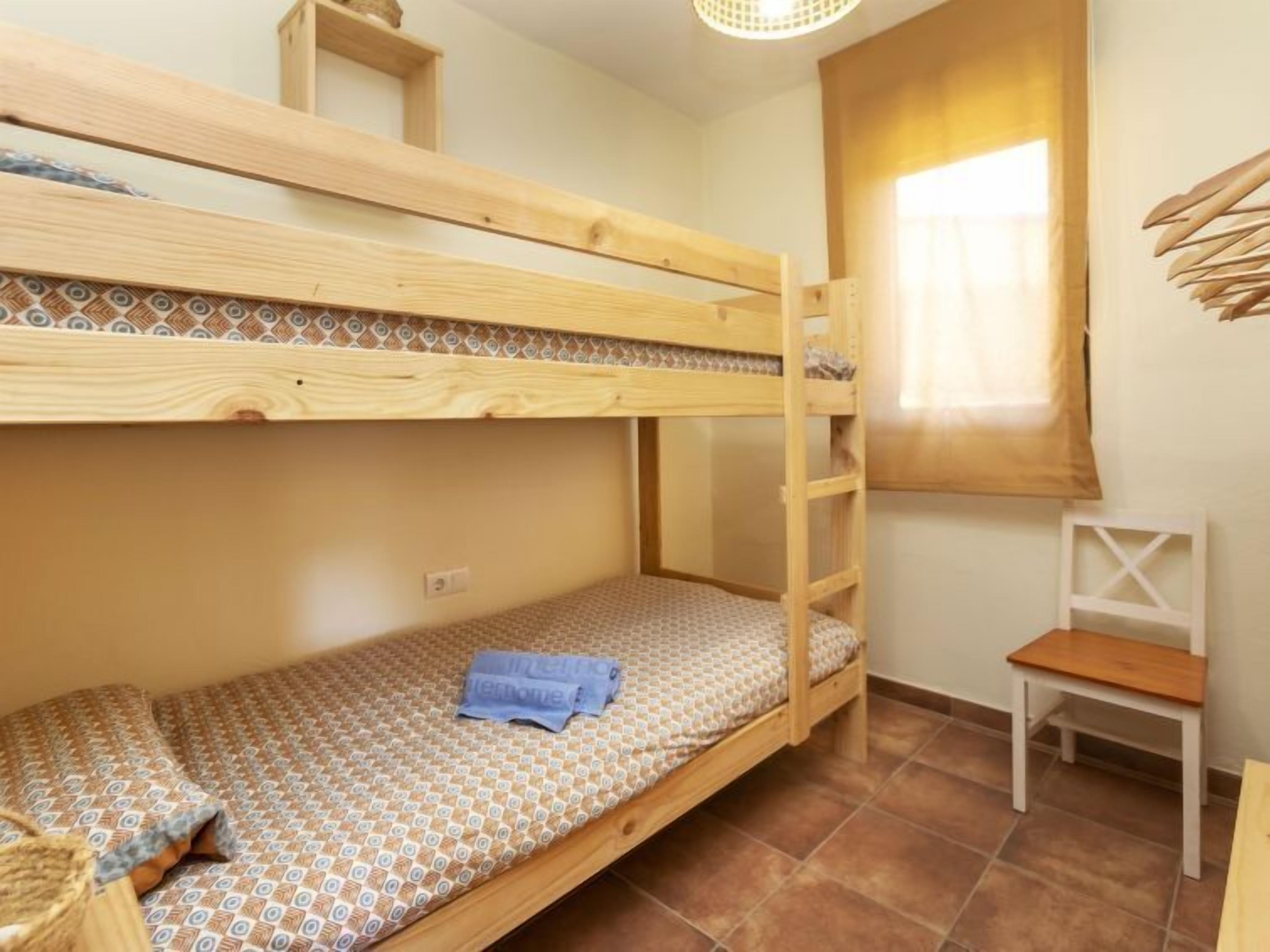 A bunk bed room with a patterned mattress, a small table, and a window with curtains.