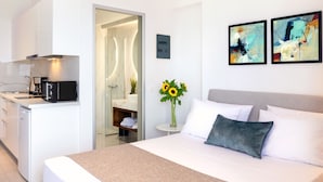 A modern hotel room with a bed, a small bedside table with a vase of sunflowers, and a view into the bathroom. - Creta Sun, Studio 104 Sea view (Rethymno)