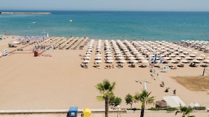 A beach with rows of umbrellas and sun loungers, a clear sky, and the sea in the background. - Creta Sun, Studio 104 Sea view (Rethymno)