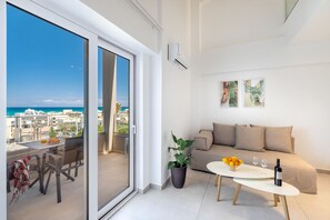 A modern living room with a balcony, a sofa, a coffee table, and a potted plant. - Creta Sun, Mezzanine 203 Sea view (Rethymno)