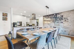 Una cocina moderna con armarios blancos, una campana extractora de acero inoxidable y un comedor con una mesa de madera dispuesta para seis.