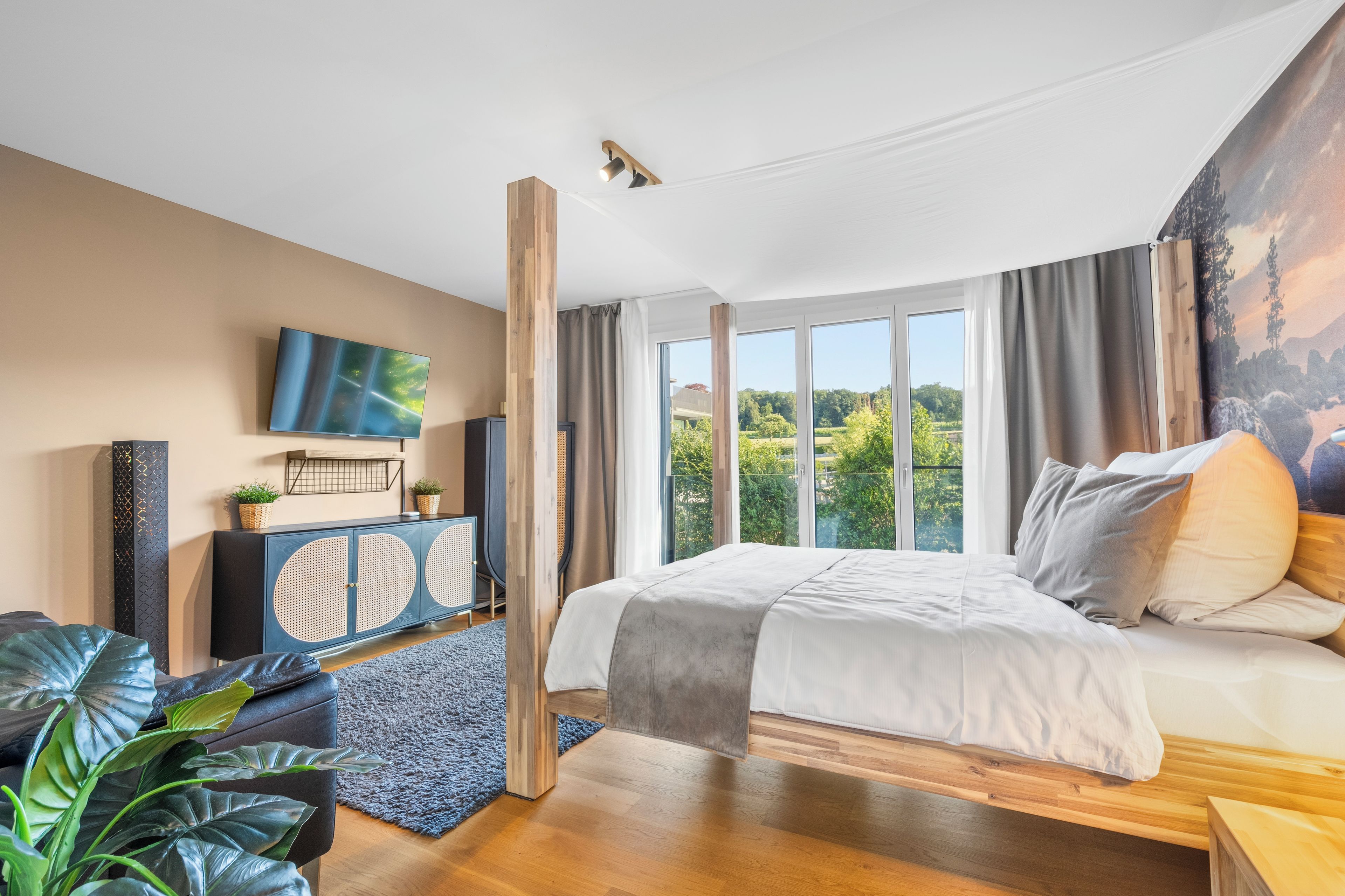 Une chambre moderne avec un grand lit, un téléviseur et une vue sur la verdure environnante.