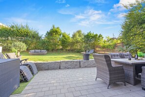 Un área de patio al aire libre con mobiliario de mimbre, una pared de piedra y un césped.
