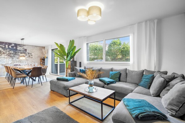 A modern living room with a grey sofa, a coffee table, and a dining area with chairs and a table.