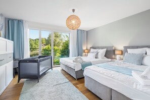 Ein modernes Schlafzimmer mit zwei Betten, einem Schlafsofa und Blick auf Grünfläche.