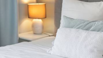 Ein ordentlich bezogenes Bett mit weißer Bettwäsche und Kissen, eine Nachttischlampe und ein Nachttisch.