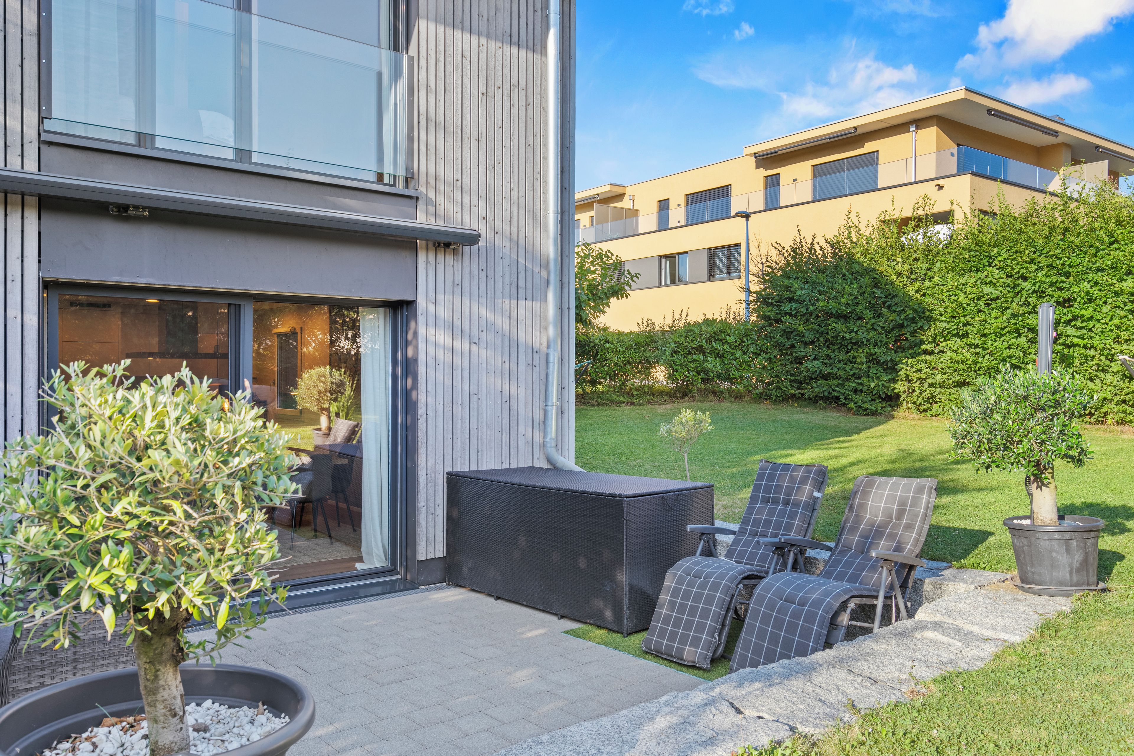 Ein modernes Gebäude mit einer Terrasse, Sitzgelegenheiten im Freien und einem kleinen Baum.