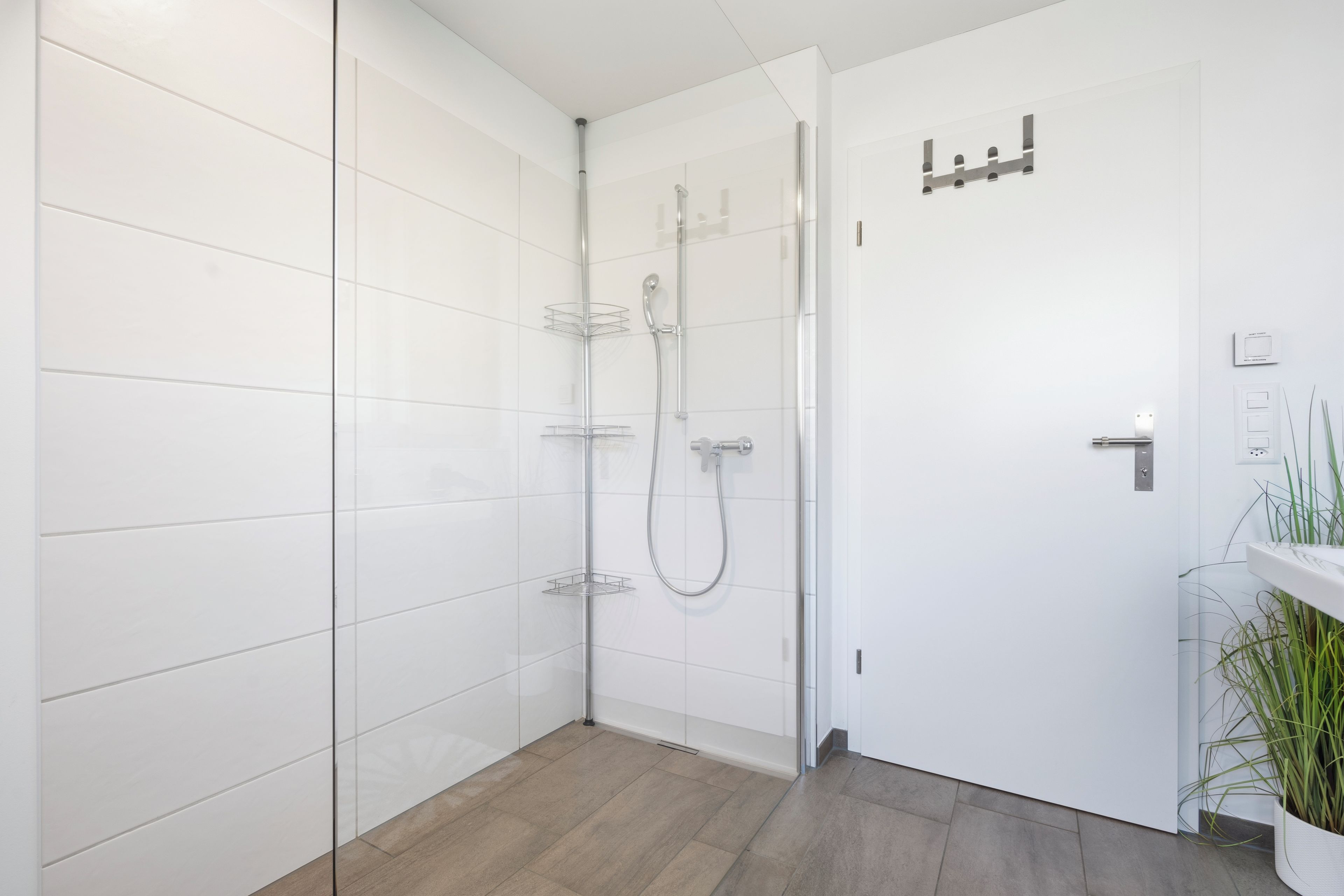 Une salle de bain moderne avec des murs recouverts de carreaux blancs, une douche avec une porte en verre et un plancher en bois.