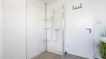 Une salle de bain moderne avec des murs recouverts de carreaux blancs, une douche avec une porte en verre et un plancher en bois.