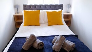 Un lit avec deux oreillers jaunes, une couvre-lit bleu foncé et deux serviettes enroulées posées sur le lit.