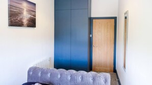 Une pièce avec une grande armoire bleue, une porte en bois, un tableau encadré au mur et un banc recouvert d’un tissu gris.