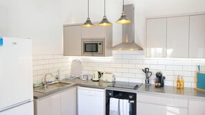 Une cuisine moderne avec des armoires blanches, un four à micro-ondes encastré, un lave-vaisselle et des luminaires suspendus.