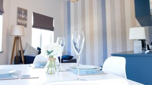 Un coin repas avec une table dressée pour deux personnes, agrémenté d’un verre à vin en verre transparent et d’un vase contenant des fleurs blanches.