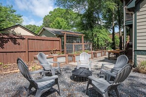 Een achtertuin met een terras, Adirondack-stoelen, een ronde tafel en een houten omheining.
