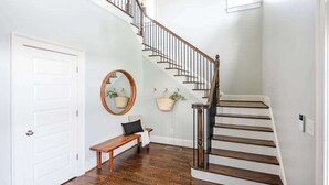 A staircase with wooden steps and a metal railing, a white door, a bench, a mirror, and two hanging baskets on the wall.