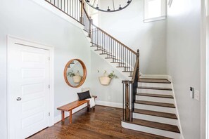 A staircase with wooden steps and a metal railing, a white door, a bench, a mirror, and two hanging baskets on the wall.