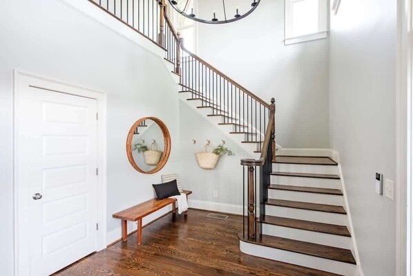 A staircase with wooden steps and a metal railing, a white door, a bench, a mirror, and two hanging baskets on the wall.