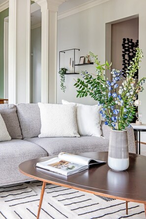 Een moderne woonkamer met een grijze modulaire bank, een ronde salontafel met een tijdschrift, en een witte vaas met bloemen.